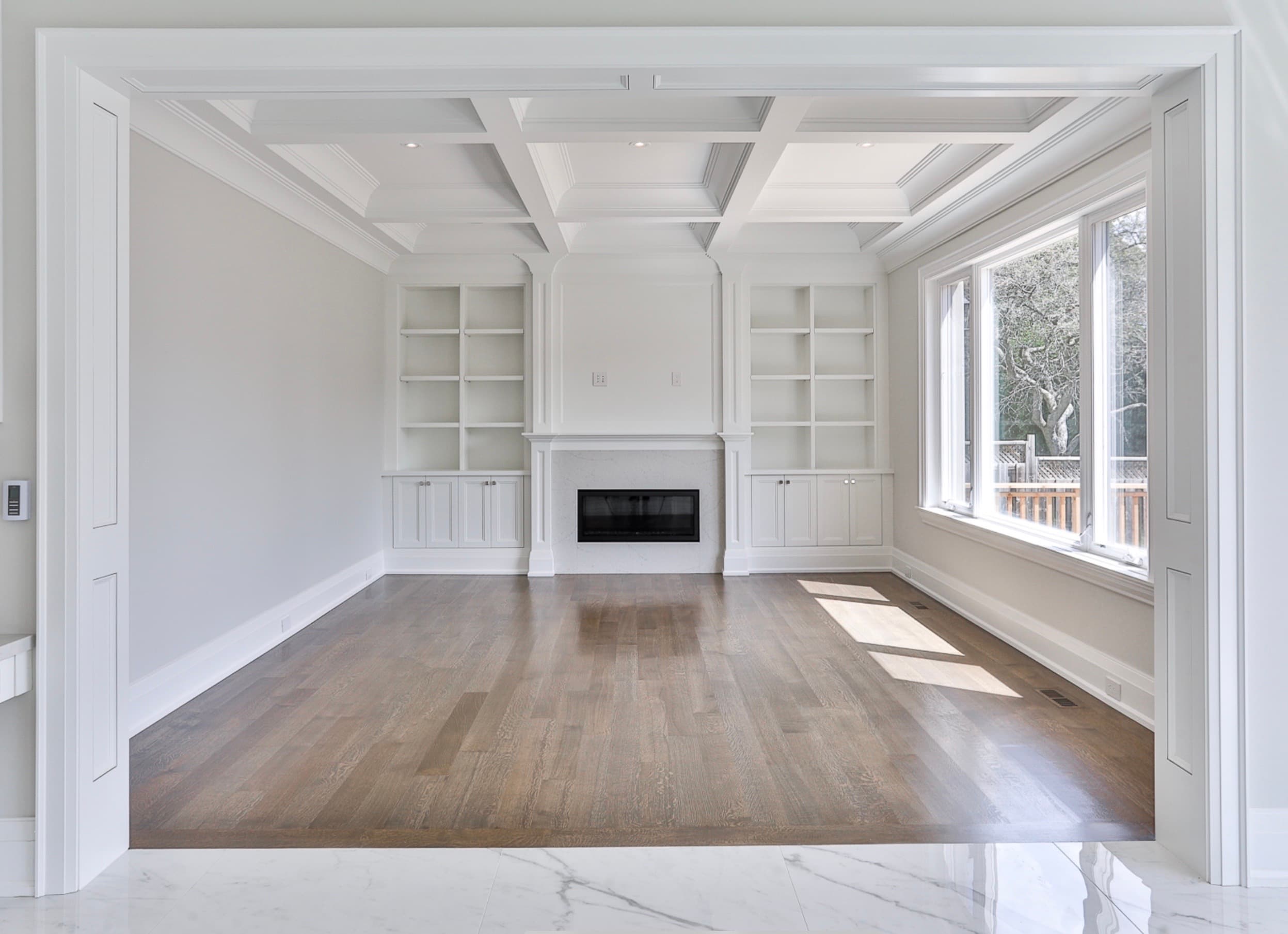White built-in shelving flanking a linear fireplace under a coffered ceiling, Uniline project